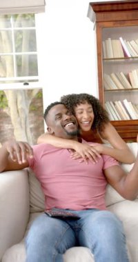 Dikey video: Kanepede oturan gülümseyen çift, evde birlikte vakit geçirip kucaklaşıyorlar. Aşk, ilişki, birliktelik, mutluluk, bağ, sevgi