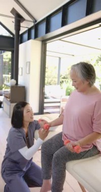 Dikey video: Ev egzersizi seansı rehberliği, fizyoterapistin yaşlı kadına halterli yardım etmesi. Sağlık, refah, yaşlılık, yardım, rehabilitasyon, eğitim