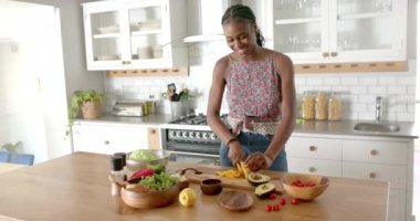 Çiçekli bluz giyen Afro-Amerikalı genç kadın evde, mutfakta sebze kesiyor. Saçlarını ördü, gülümsüyor ve bir salata hazırlıyor, değişmemiş, ağır çekimde.