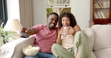 Televizyon seyredip gülen, koltukta oturan patlamış mısır kaseli bir çift. Rahatlama, eğlence, oturma odası, eğlence, atıştırmalık, mutluluk