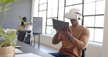 VR kulaklık kullanarak, Afrikalı Amerikalı adam modern ofis ortamında tabletle etkileşime geçiyor. Teknoloji, sanal gerçeklik, iş, yenilik, dijital, işyeri
