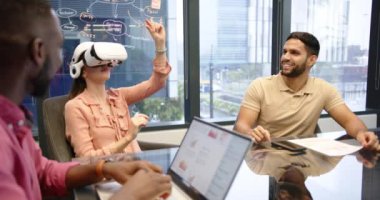 VR kulaklığı kullanarak, ofiste çok ırklı iş arkadaşlarıyla buluşan bir kadın, projeyi tartışıyor. Sanal gerçeklik, takım çalışması, işbirliği, iş dünyası, teknoloji, beyin fırtınası