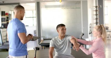 Fizyoterapist kol egzersizlerinde adama yardım ediyor, başka bir terapist de not alıyor. Fizyoterapi, rehabilitasyon, sağlık, sağlık, yardım, klinik, değişmemiş, yavaş çekim