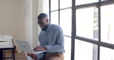 Gülümseyen iş adamı dizüstü bilgisayar tutuyor ve modern ofisin penceresinden dışarı bakıyor. profesyonel, kendinden emin, yönetici, çalışma alanı, teknoloji