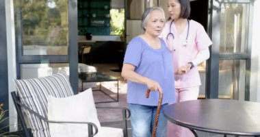 Bastonlu, pembe önlüklü, gülümseyen yaşlı Asyalı kadına yardım etmek. yaşlılar, bakım, yardım, sağlık, destek