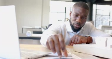 Afrika kökenli Amerikalı işadamı ofisteki mimari modeli ölçüyor ve üzerinde çalışıyor. Mimarlık, tasarım, mühendislik, planlama, plan, inşaat
