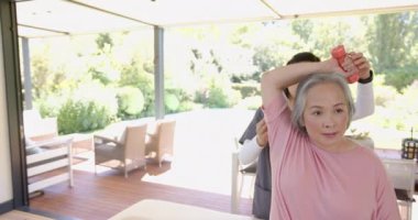 Kıdemli Asyalı kadın, evde fizyoterapistin yardımıyla halterli egzersiz yapıyor. Egzersiz, fitness, fizyoterapi, sağlık, rehabilitasyon, destek