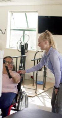 Dikey video: Engelli rehabilitasyonunda, tekerlekli sandalyedeki kadın terapistin yardımıyla egzersiz yapıyor. Fizyoterapi, rehabilitasyon, egzersiz, sağlık, hareketlilik, terapi, yavaş çekim