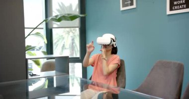 VR kulaklık kullanan, modern ofis ortamında masa başında oturan bir kadın. Teknoloji, sanal gerçeklik, yenilik, çağdaş, işyeri, iş dünyası