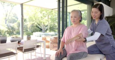 Fizyoterapist, evde terapi seansında yaşlı Asyalı kadına kol egzersizleri yaptırıyor. Rehabilitasyon, sağlık, fizyoterapi, egzersiz, yaşlılık, iyileşme