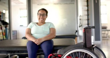 Rehabilitasyon merkezinde tekerlekli sandalyeyle terapi masasında oturan gülümseyen kadın. Sağlık, iyileşme, fizyoterapi, fizik tedavi, egzersiz, refah, değişmemiş, yavaş çekim