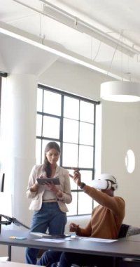 Dikey video: VR kulaklık kullanan erkek, modern ofiste tablet tutan kadınla işbirliği yapıyor. Teknoloji, sanal gerçeklik, işbirliği, iş dünyası, takım çalışması, yenilik