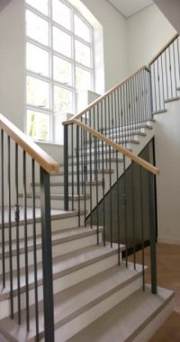 Dikey video: Parlak evdeki ahşap korkuluklu ve geniş pencereli modern merdiven. İç mimari, tasarım, çağdaş, ev dekorasyonu, doğal ışık, yavaş çekim