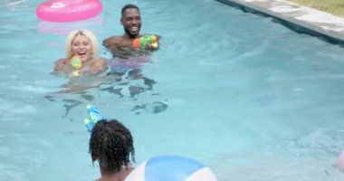 Çeşitli aileler su tabancaları ve plaj topuyla bilardo oynuyorlar. Şişme oyuncaklarla dolu arka bahçe havuzu ve yemyeşil çimenler eğlenceli ve canlı bir atmosfer yaratıyor, değiştirilmemiş, yavaş çekim