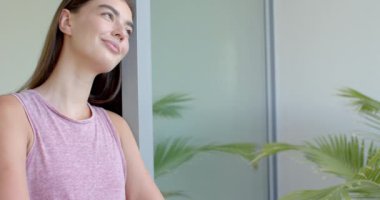 Pencereden dışarı bakan, pembe kolsuz tişörtlü, fotokopi çeken beyaz bir kadın. Uzun kahverengi saçları, açık tenli, ve yavaşça gülümsüyor, değişmeden, yavaş çekimde.