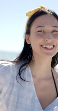 Dikey video: Gülümseyen kadın plajda güneşli bir günün tadını çıkarıyor, günlük kıyafetlerini giyiyor. Tatil, eğlence, rahatlama, açık hava, moda, yaşam tarzı, yavaş çekim