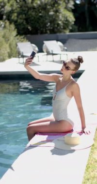 Dikey video: Güneşli bir günde bilardo masasında oturmuş selfie çeken mayolu genç kız. Tatil, yaz, eğlence, açık hava, yaşam tarzı, oyuncu, yavaş çekim