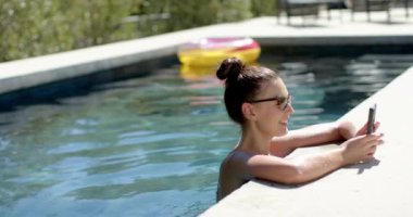 Beyaz kadın havuzda dinleniyor, güneş gözlüğü takıyor, fotokopi çekiyor. Saçları topuz gibi ve güneşli havanın tadını çıkarıyor, değişmemiş, ağır çekim.