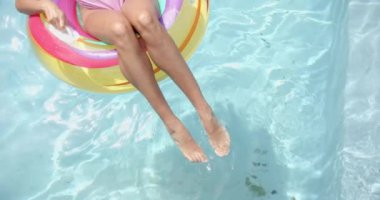 Evdeki şişme yüzükle havuzda rahatlayan melez bir genç kadın. Kopya alanı. Pembe oje sürmüş, açık kahverengi tenli, değişmemiş, ağır çekimde suyun tadını çıkarıyor.