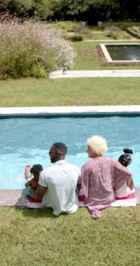 Dikey video: Aile havuz başında oturuyor, ebeveynler dışarıda güneşli bir günün tadını çıkarıyor. Havuz başı, yaz, boş zaman, bağlanma, tatil, yavaş çekim