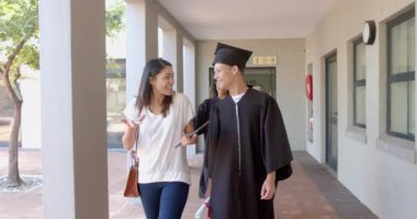 Mezuniyet kıyafeti giymiş melez bir çocuk lisede iki kadınla yürüyor. Genç mezunumuzun bu anı genç bir kız ve melez bir kadınla paylaştığı kutlama havası..