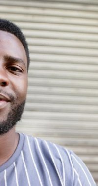 Dikey video: Çizgili tişörtlü gülen adam kafenin önünde duruyor, günün tadını çıkarıyor. Kentsel, yaşam tarzı, rahatlama, rahatlama, açık hava, mutluluk, yavaş çekim