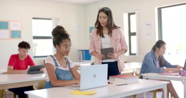 Genç melez bir kadın lisede bir sınıfta öğretmenlik yapıyor. Öğrenciler yavaş çekimde öğrenme deneyimlerinin bir parçası olarak teknolojiyle ilgilenirler..