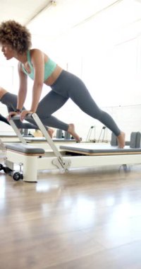 Dikey video: yoga stüdyosunda pilates reformatöründe egzersiz yapan Afrikalı Amerikalı kadın. Spor, egzersiz, sağlık, sağlıklı yaşam tarzı, spor, egzersiz, ağır çekim