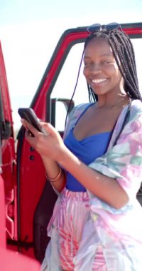 Dikey video: Güler yüzlü kadın yol gezisinde kırmızı arabanın yanında duruyor. Seyahat, macera, teknoloji, yaşam tarzı, özgürlük, tatil, mutluluk, yavaş çekim