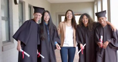 Çeşitli mezunlar başarılarını kutluyor. Şapkalı ve cüppeli gülümseyen öğrenciler lise seremonisinde diploma taşıyorlar, ağır çekimde..