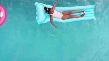 Mavi havuzda dinlenen Afro-Amerikan bir kızın robot resmi, kopyalama alanı. Güneş gözlüğü takıyorum, güneşli günün tadını çıkarıyorum, açık mavi arka planla çevrili. Usulca süzülür, su parıldar, değişmez.