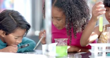 Okulda, bir grup genç öğrenci sınıfta bir kimya deneyi yapıyorlar. Çeşitli grupta Afro-Amerikan ve Asyalı çocuklar var. Renkli test tüplerine odaklanmış, değiştirilmemiş.