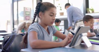 Çift ırklı kız okuldaki tabletine odaklanmış. Sınıf ortamında teknolojiyle ilgileniyor, ağır çekimde..