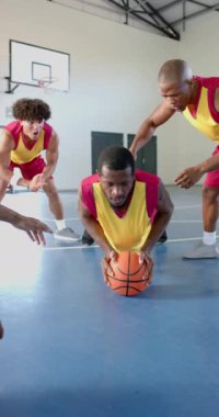 Dikey video: Basketbol oynamak, takım arkadaşları spor salonunda tezahürat yaparken erkek sporcu top için dalmak. Spor, rekabet, takım çalışması, aksiyon, spor salonu, tezahürat