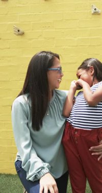 Bir okul bahçesinde, genç bir melez öğrenci gülümseyen annesinin yanında duruyor. Her ikisi de şık güneş gözlüğü takıyor, anne mavi bluz giyiyor, çocuk çizgili bluz ve kırmızı pantolon giyiyor..