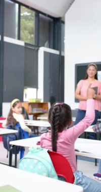 Dikey video: Okulda, kız soru sormak için elini kaldırırken öğretmen gülümsüyor. Eğitim, sınıf, öğrenim, öğretim, öğrenci, katılım, yavaş çekim