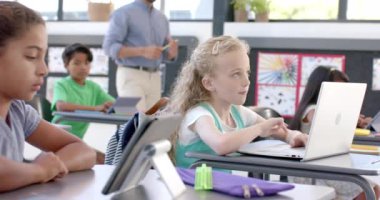 Okulda dizüstü bilgisayarı olan beyaz bir kız. Dersiyle meşgul görünüyor, elini kaldırarak bir soru soruyor, ağır çekimde..