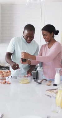Dikey video: Mutfakta bir çift birlikte kahvaltı hazırlıyor, yumurta çırpıyor ve baharat ekliyor. Aşçılık, yerli, birliktelik, ağır çekim