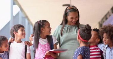 Okulda elinde kitaplarla bir grup öğrenciyle gülümseyen bir öğretmen. Eğitim, öğrenim, sınıf, çeşitlilik, akademik, takım çalışması, değiştirilmemiş, yavaş çekim