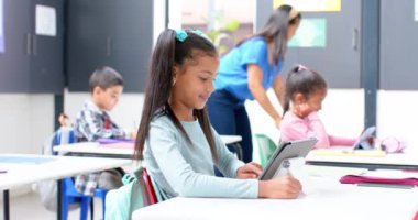 Okulda, masada tablet kullanan bir kız, dijital öğrenme aktivitelerine odaklanıyor. Eğitim, okula dönüş, eğitim, çocukluk, teknoloji, sınıf, değiştirilmemiş, yavaş çekim