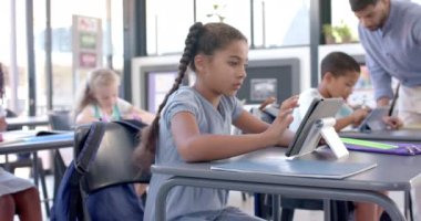 Çift ırklı kız okuldaki tabletine odaklanmış. Modern bir sınıf ortamında, yavaş çekimde dijital bir ders veriyor..