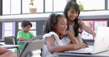 Çift ırklı kızlar bir sınıfta dizüstü bilgisayarla okul projesinde yer alıyorlar. Aydınlık bir sınıfta, ağır çekimde bir dizüstü bilgisayarda iş birliği yapıyorlar..