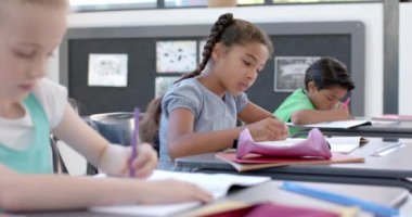 İki ırklı kız okuldaki bir sınıf ortamında kafa yoruyor. Öğrenciler ödevlerini yapıyorlar, tipik bir okul ortamı sergiliyorlar, yavaş çekimde..