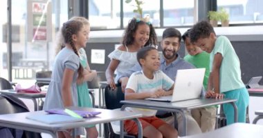 Sınıftaki bir okulda çeşitli öğrencileri olan bir öğretmen. Dizüstü bilgisayarın etrafında eğlenceli bir öğrenme aktivitesiyle meşguller, ağır çekimde..