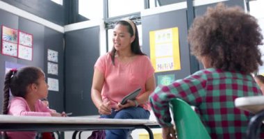 Okulda, öğretmen sınıf masasında öğrencilere ödevlerinde yardım ediyor. Eğitim, öğrenim, öğrenim, yardım, takım çalışması, çocuklar, değiştirilmemiş, yavaş çekim