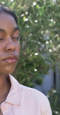 Dikey video: Bahçede dikilen kadın ciddi ve düşünceli görünüyor. Doğa, tefekkür, yalnızlık, yeşillik, barışçıl, düşünceli, yavaş çekim