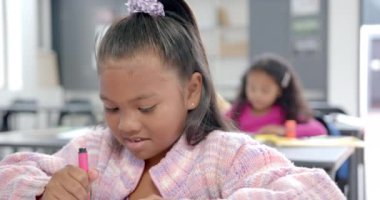 Okulda, sınıftaki işlerine odaklanan bir grup genç öğrenci var. İki melez kız ve günlük kıyafetler giyen bir Afrikalı Amerikalı erkek, yazı ve çizim, değişmemiş, yavaş çekim.