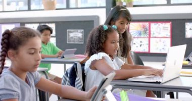 Çift ırklı kızlar bir sınıfta dizüstü bilgisayarla okul projesinde yer alıyorlar. Canlı bir sınıf ortamında, ağır çekimde dizüstü bilgisayar kullanarak iş birliği yapıyorlar..