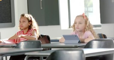 Kafkasyalı kız merakla bakarken, melez kız okuldaki derslerine odaklanmış. Okulda bir sınıf ortamında oturuyorlar, farklı aktivitelerle meşguller, ağır çekimde..