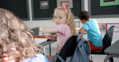 Sarışın, kıvırcık saçlı beyaz kız okuldaki bir sınıfta gülümsüyor. Pembe bir gömlek giyiyor ve kızıl saçlı bir aksesuarı var, gençlik neşesini yakalıyor..
